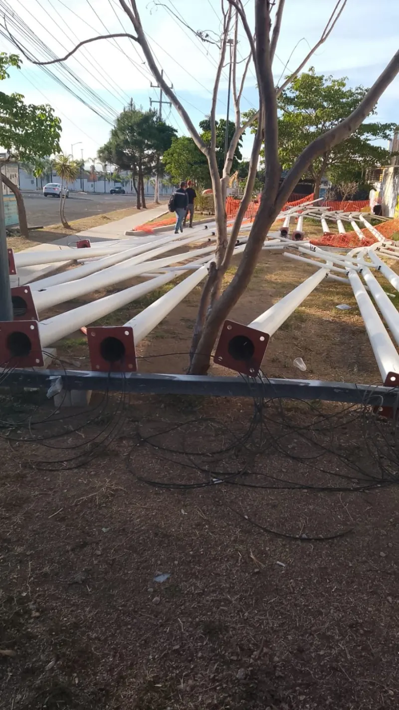 Poste de alumbrado vertical junto a una grúa sobre camión y vehículos estacionados.