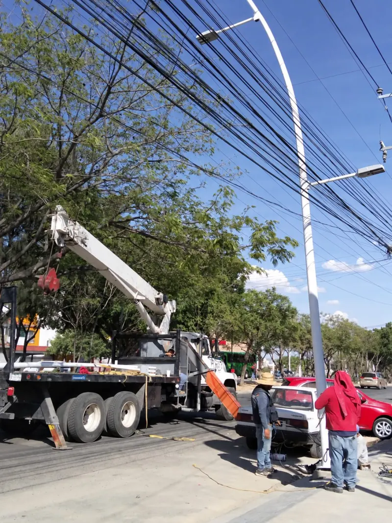 Postes blancos con placas de base y cableado, acomodados horizontalmente junto a la banqueta.