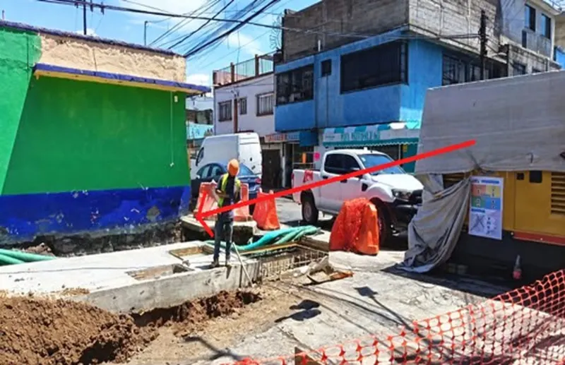 Trabajador junto a una base de concreto y excavaciones, con el equipo amarillo al fondo.