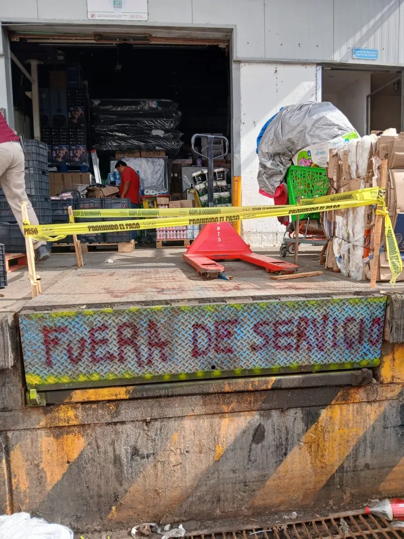 Andén delimitado con cinta, un patín hidráulico y mercancía junto a la rampa.