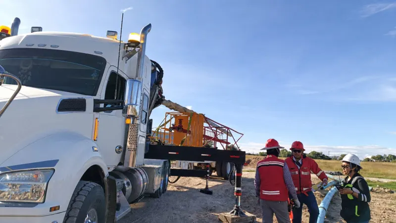 Estructura metálica roja suspendida de una grúa sobre una plataforma, con escalera y barandales amarillos.